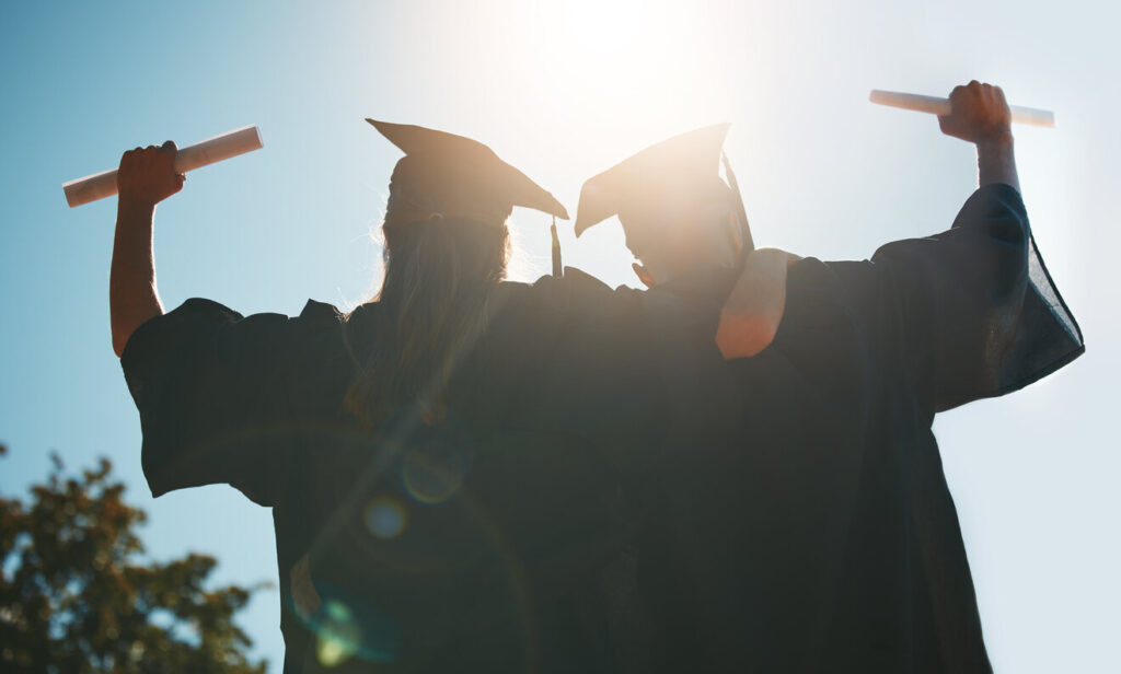 Two graduates in caps and gowns with diplomas raised high against a sunny sky, symbolizing academic achievement and the promising future for applicants of Glen Larson Law’s 2025 College Scholarship.